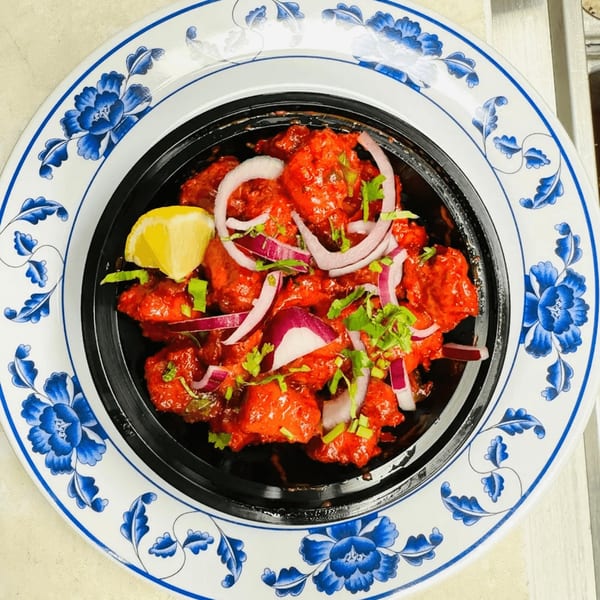 Bright red Indian chicken dish, garnished with red onions, cilantro, and a lemon wedge, on a blue and white plate.