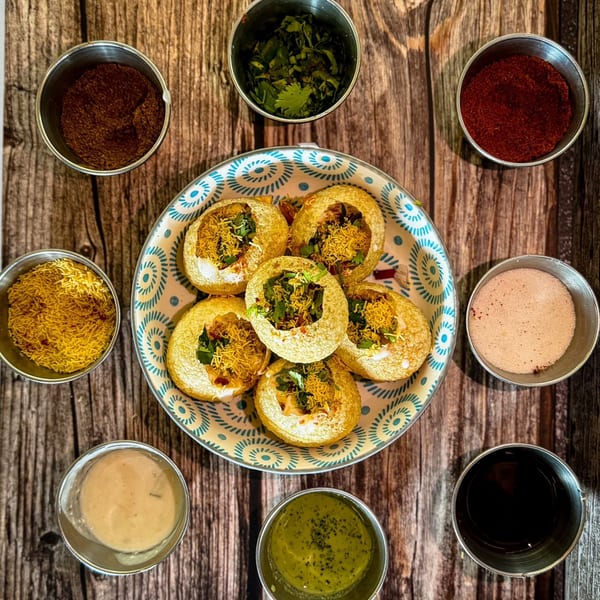 Overhead view of Indian pani puri on a plate surrounded by small bowls of spices and sauces.