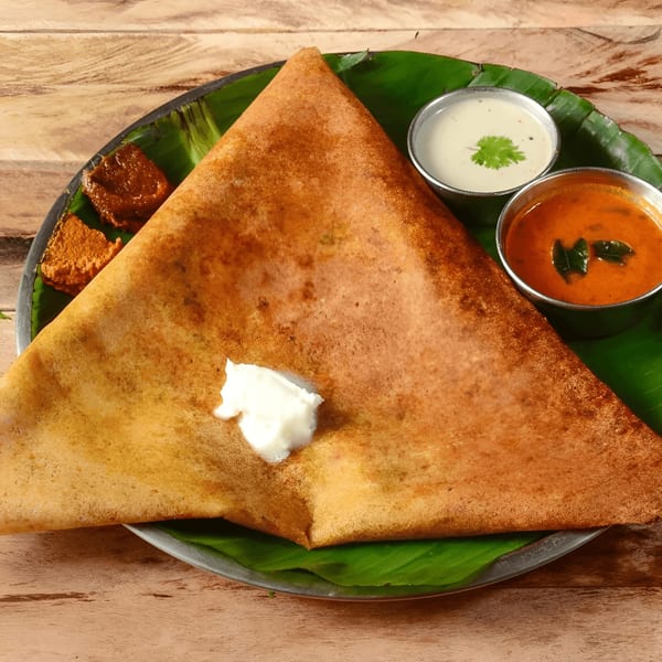 A triangular dosa with white butter, served with chutney and sambar on a banana leaf.