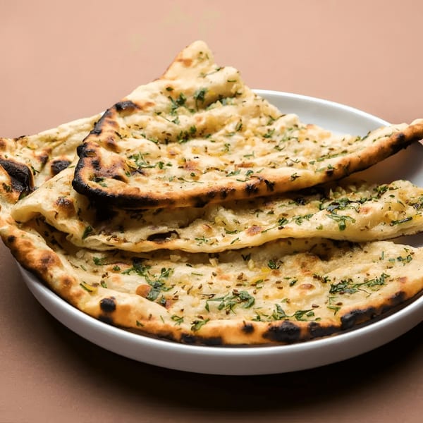 Freshly baked garlic naan bread, garnished with herbs and spices, served on a white plate.