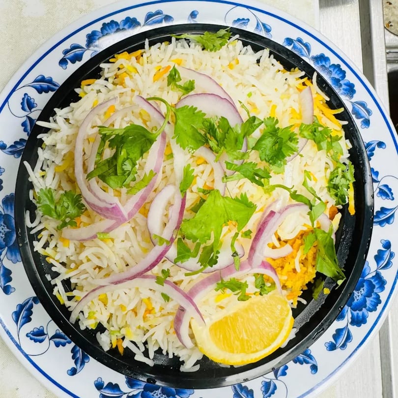 Indian biryani with white and yellow rice, red onions, cilantro, and a lemon wedge.