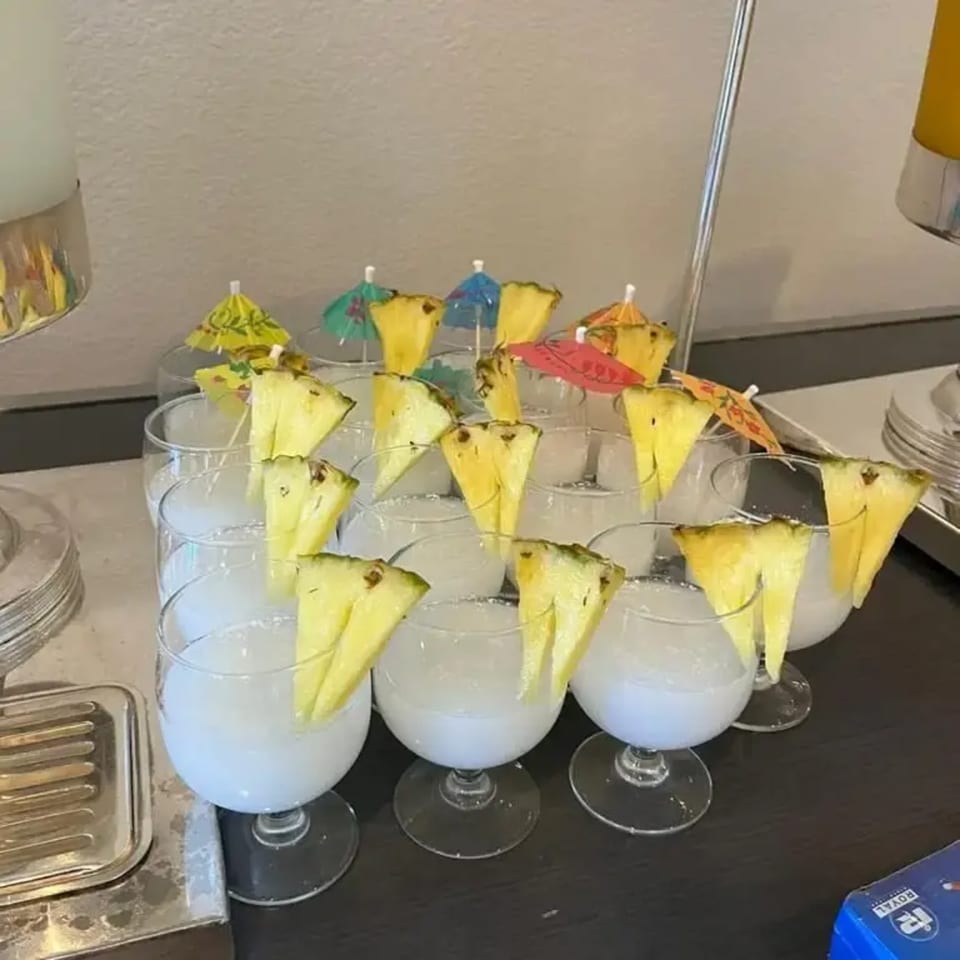 Row of cocktails garnished with pineapple slices and colorful paper umbrellas on a dark surface.
