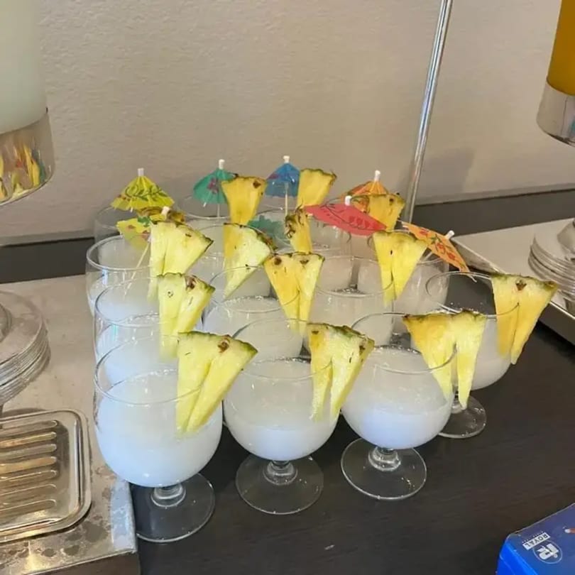 Row of cocktails garnished with pineapple slices and colorful paper umbrellas on a dark surface.