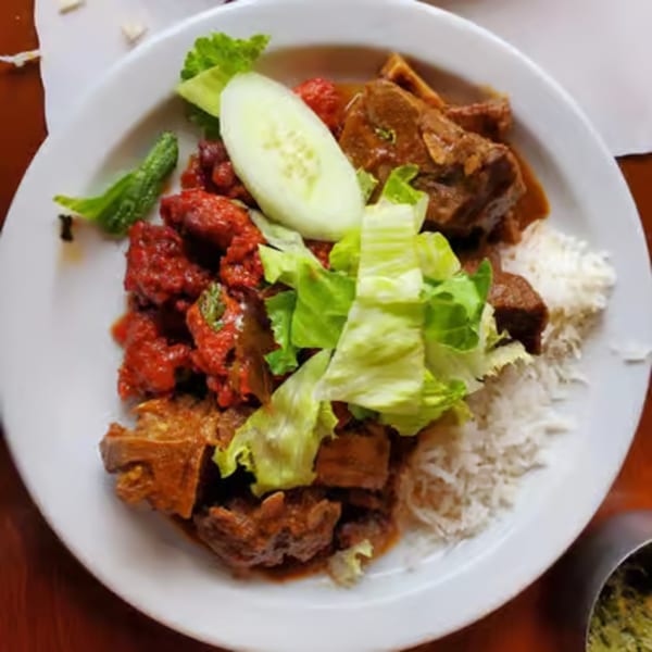 A white plate with Indian food, including red chicken tikka, brown meat, rice, and salad.