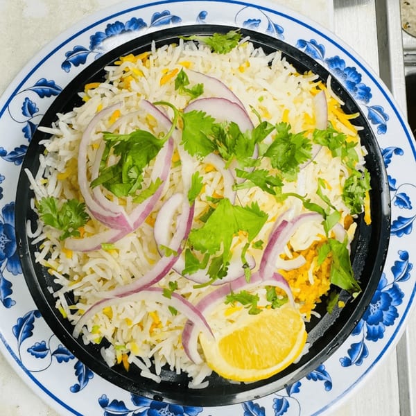 Indian biryani with white and yellow rice, red onions, cilantro, and a lemon wedge.