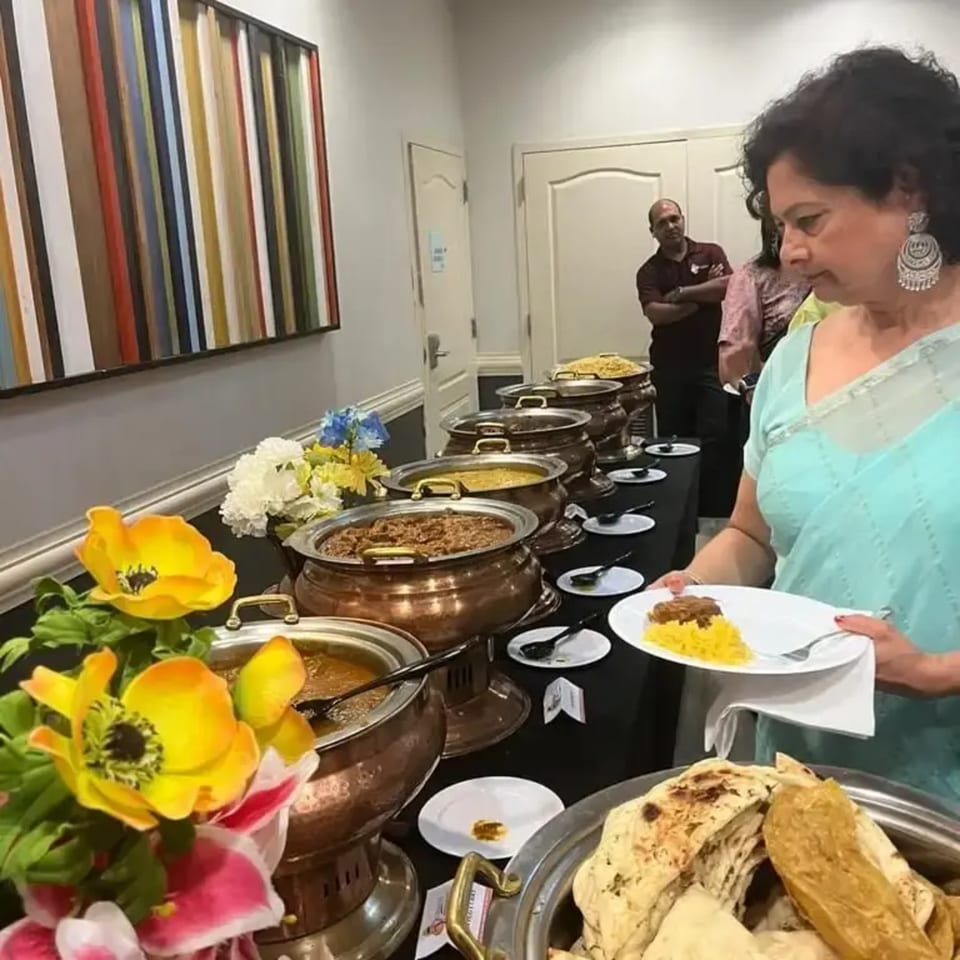 A woman in a light blue sari serves herself Indian food from a buffet line at 5th Element.