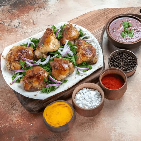 Indian grilled chicken pieces with herbs, onions, sauce, and spices in bowls on a wooden board.