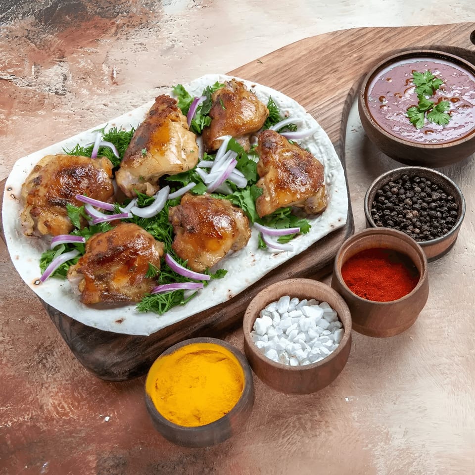 Indian grilled chicken pieces with herbs, onions, sauce, and spices in bowls on a wooden board.