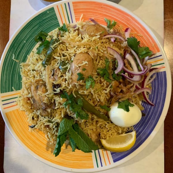 Chicken Biryani with rice, chicken, red onions, cilantro, mint, a hard-boiled egg, and lemon.