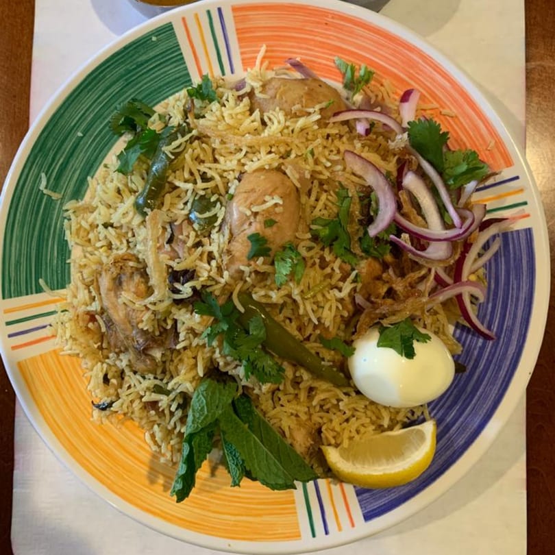 Chicken Biryani with rice, chicken, red onions, cilantro, mint, a hard-boiled egg, and lemon.