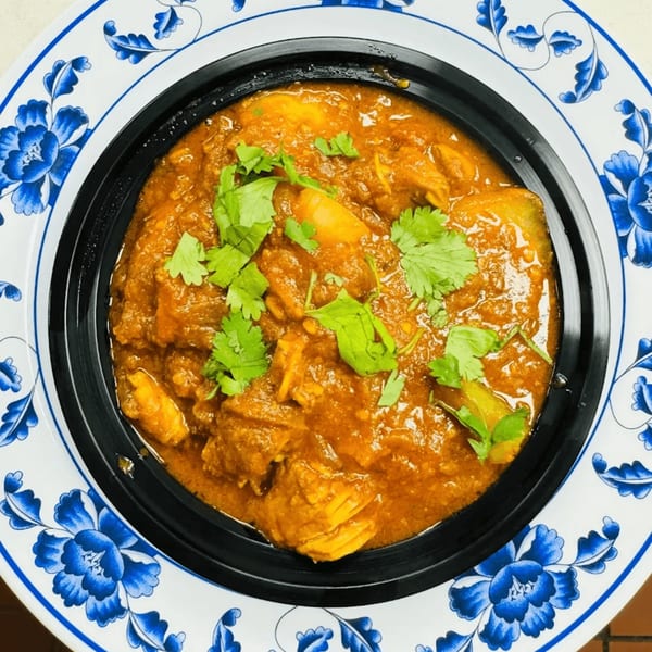 A close-up of Indian chicken curry with cilantro in a black bowl on a blue and white plate.